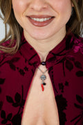 Donna indossa collana con ciondolo doppia maschera in metallo con corallo rosso e perla nera su camicia bordeaux
